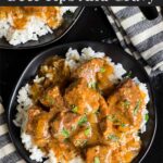 Slow cooker beef tips and gravy over cooked rice on a dark plate on a dark surface.