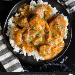 Slow cooker beef tips and gravy over cooked rice on a dark plate on a dark surface.