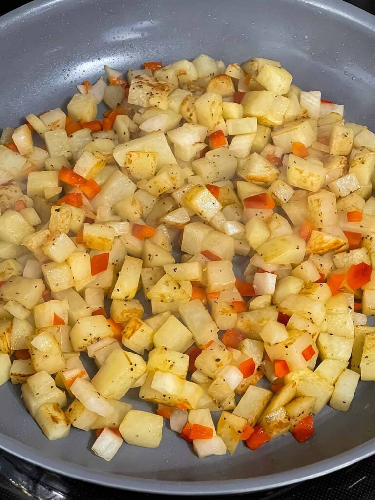 Potatoes with onions and red bell pepper in a skillet.