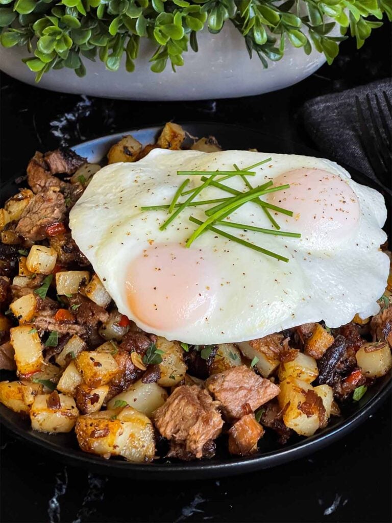 Smoked brisket hash with sunny side eggs on top on a dark plate.