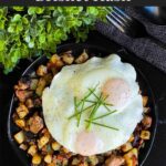 Smoked brisket hash with sunny side eggs on top on a dark plate.