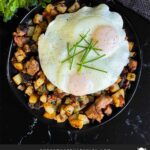 Smoked brisket hash with sunny side eggs on top on a dark plate.