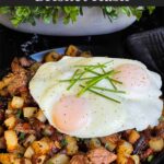 Smoked brisket hash with sunny side eggs on top on a dark plate.