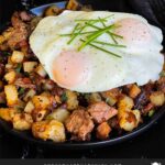 Smoked brisket hash with sunny side eggs on top on a dark plate.
