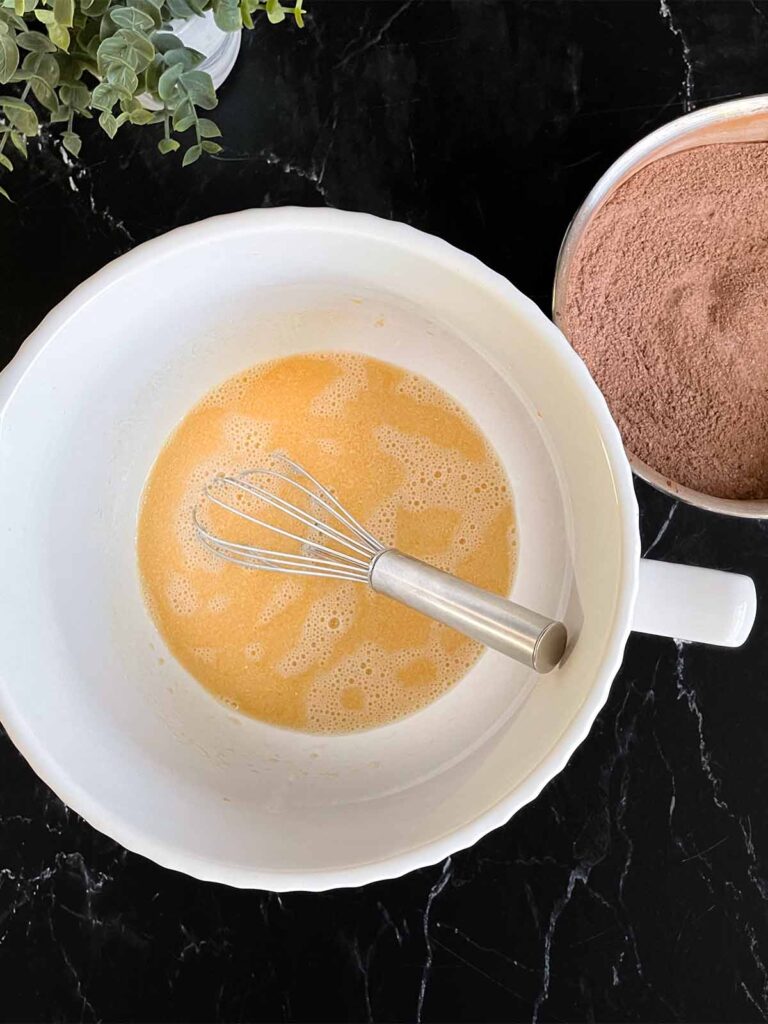 Wet ingredients for chocolate bundt cake recipe in a white mixing bowl on a dark surface.