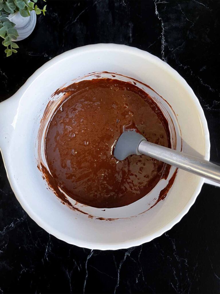 Chocolate bundt cake batter in a large mixing bowl on a dark surface.