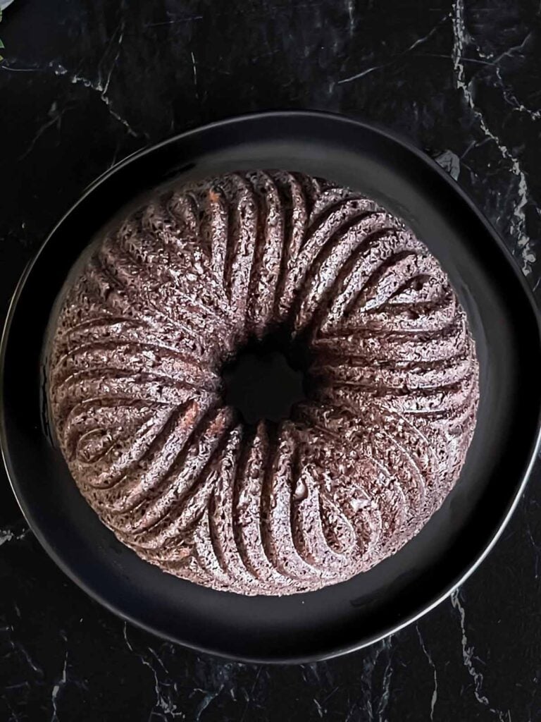 Chocolate bundt cake inverted onto a dark serving plate on a dark surface.