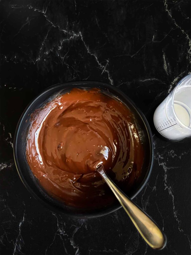 Chocolate ganache in a small dark bowl on a dark surface.