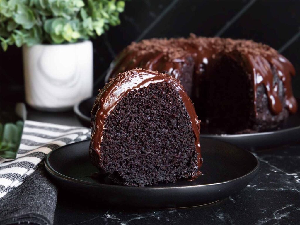 A slice of chocolate bundt cake on a dark plate.