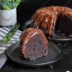 A slice of chocolate bundt cake on a dark plate.