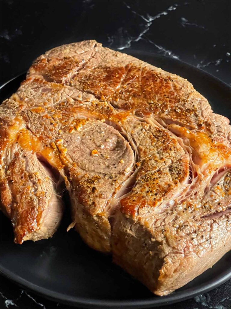 Seared chuck roast on a dark plate on a dark surface.