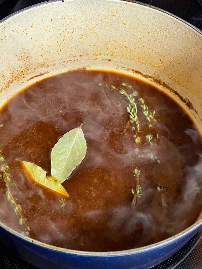 Beef broth, bay leaves, and fresh thyme added to a dutch oven for the pot roast recipe.