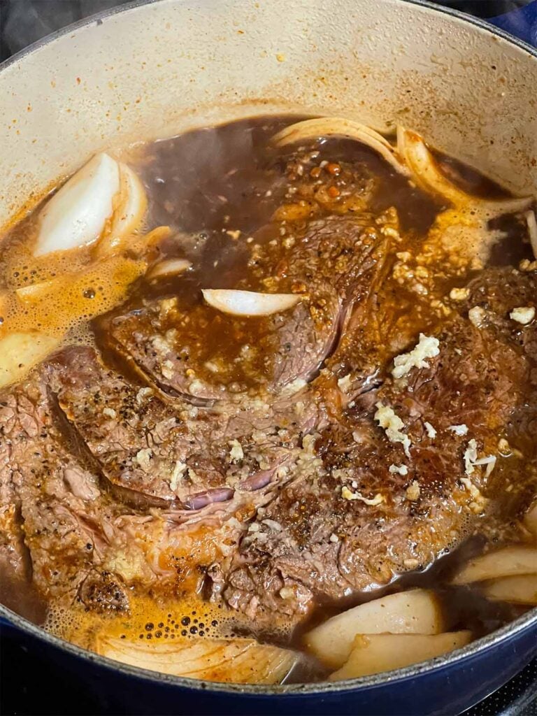 Chuck roast, onion, and garlic added to the beef broth in the dutch oven.