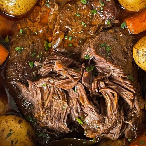 Classic pot roast with potatoes and carrots in a dutch oven on a dark surface.