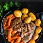 Classic pot roast with potatoes and carrots on a dark plate on a dark surface.