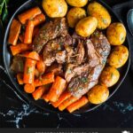 Classic pot roast with potatoes and carrots on a dark plate on a dark surface.