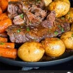 Classic pot roast with potatoes and carrots on a dark plate on a dark surface.