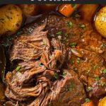 Classic pot roast with potatoes and carrots on a dark plate on a dark surface.