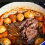 Classic pot roast with potatoes and carrots on a dark plate on a dark surface.