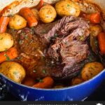 Classic pot roast with potatoes and carrots on a dark plate on a dark surface.