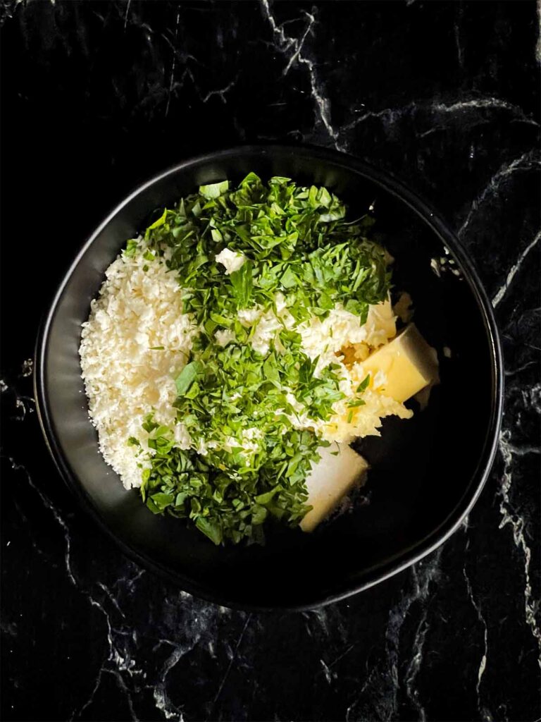 Butter and herbs in a black bowl.