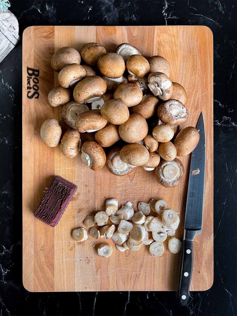 Cremini (baby bella) mushrooms cleaned and trimmed on a wooden board.