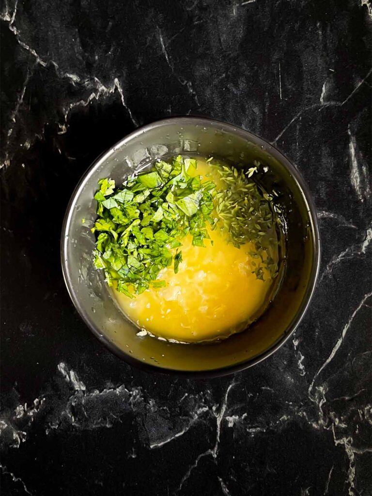 Garlic butter mixture ingredients in a dark bowl on a dark surface.