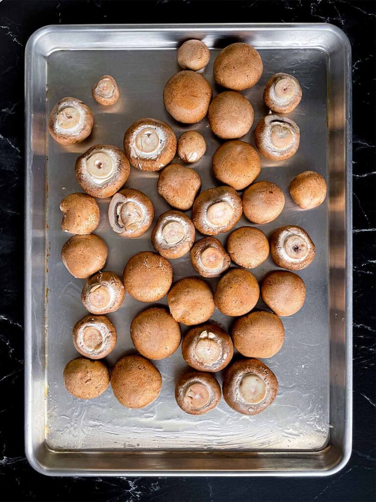 Cleaned Cremini mushrooms on an oiled baking sheet.