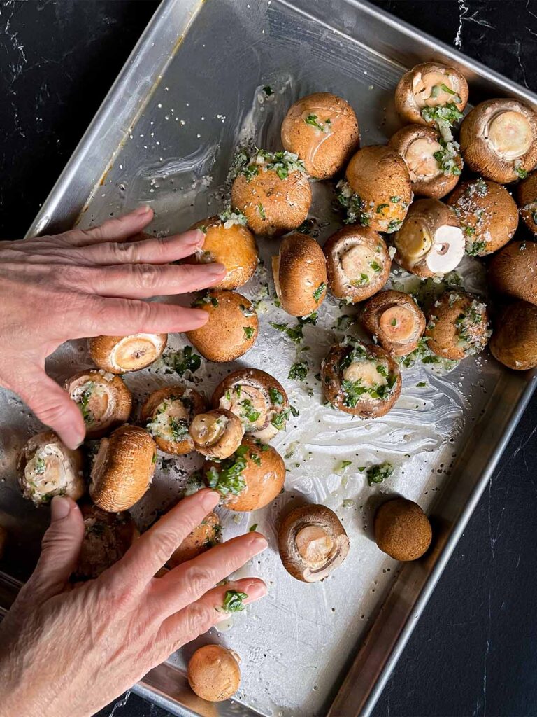 Mushrooms being tossed on the baking sheet with the garlic butter mixture.