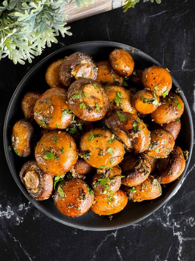 Garlic butter roasted mushrooms in a dark bowl on a dark surface.