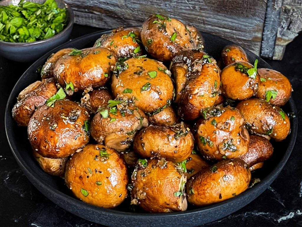 Garlic butter roasted mushrooms in a dark bowl on a dark surface.