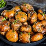 Garlic butter roasted mushrooms in a dark bowl on a dark surface.