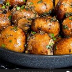 Garlic butter roasted mushrooms in a dark bowl on a dark surface.