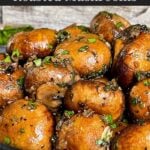 Garlic butter roasted mushrooms in a dark bowl on a dark surface.