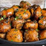 Garlic butter roasted mushrooms in a dark bowl on a dark surface.