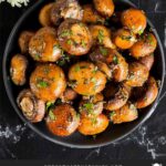 Garlic butter roasted mushrooms in a dark bowl on a dark surface.