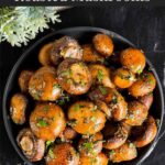 Garlic butter roasted mushrooms in a dark bowl on a dark surface.