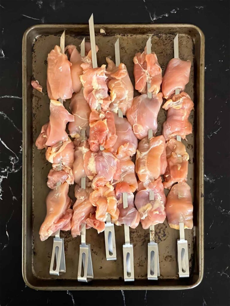 Raw chicken thighs, skewered, on a sheet pan.