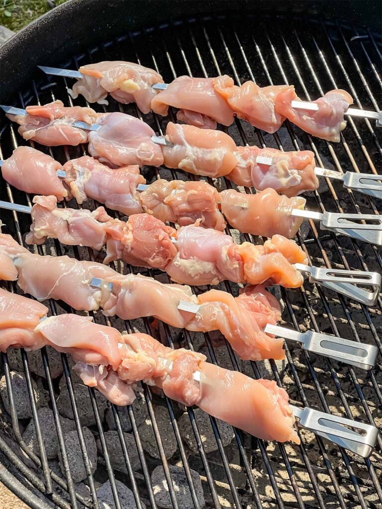 Raw chicken thighs, skewered, on the grill.