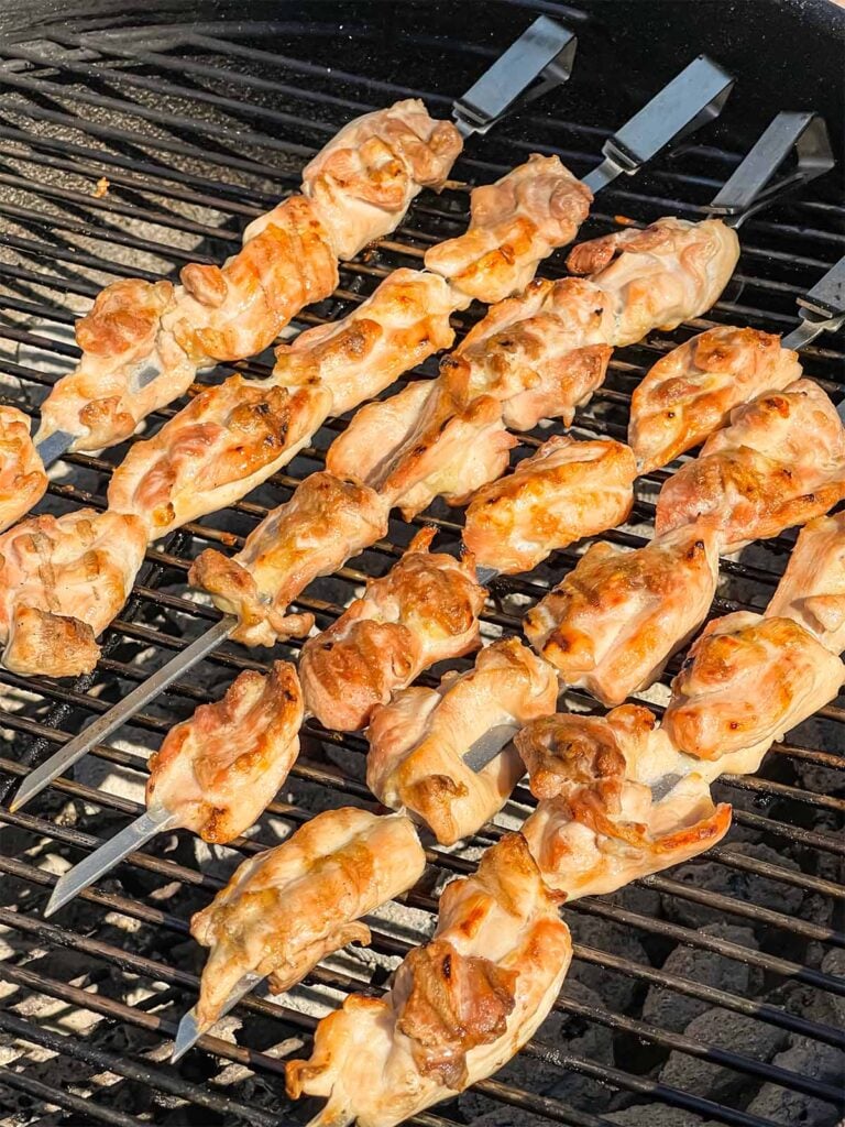 Skewered chicken thighs cooking on a grill.