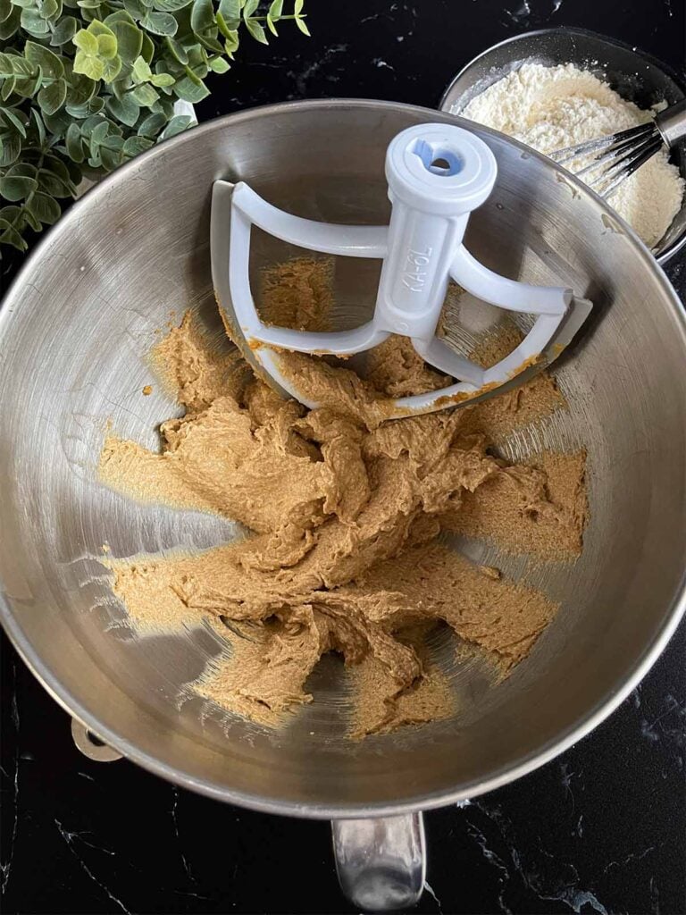 Peanut butter and unsalted butter beat together in a metal mixing bowl.