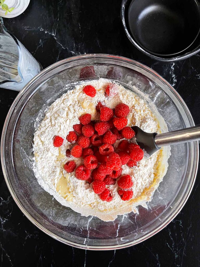 Dry ingredients and raspberries added to the wet ingredients for raspberry muffin recipe.