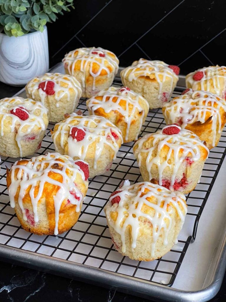 Lemon glazed raspberry muffins on a wire rack over a baking sheet lined with parchment paper.