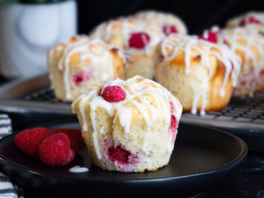 Raspberry muffin on a dark plate garnished with fresh raspberries.