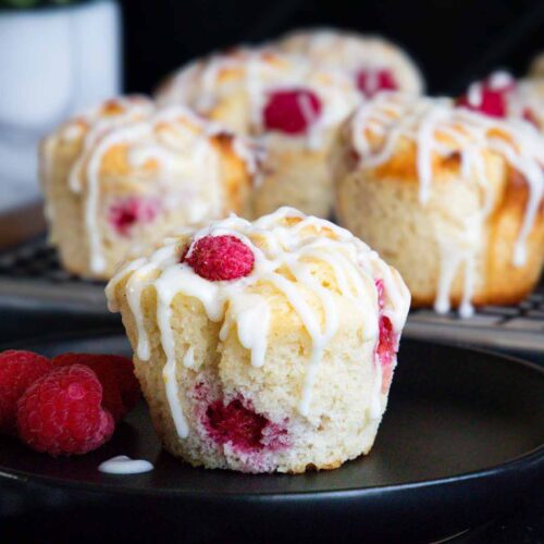Raspberry muffin on a dark plate garnished with fresh raspberries.