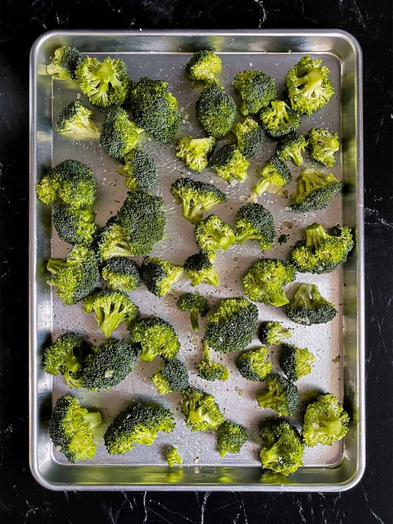 Seasoned broccoli florets on a baking sheet.