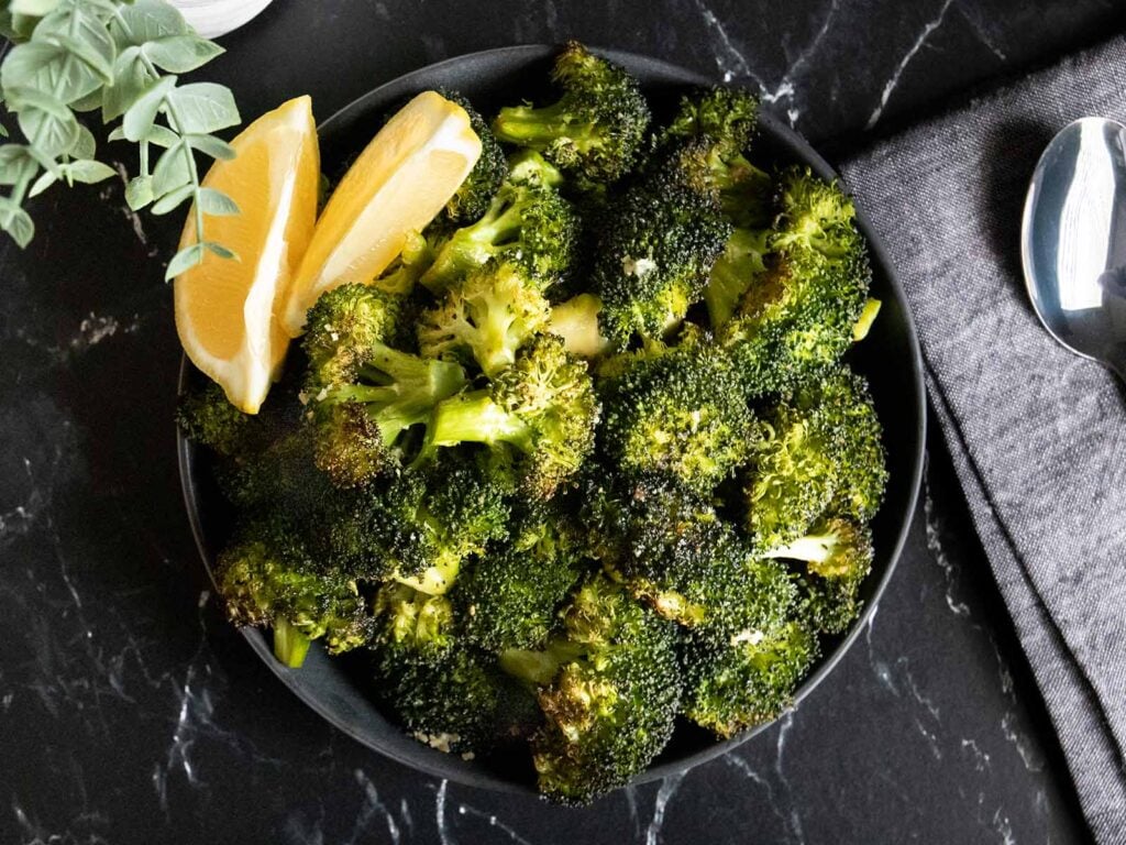 Roasted broccoli with lemon wedge garnish in a dark bowl.
