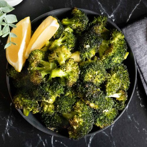 Roasted broccoli with lemon wedge garnish in a dark bowl.