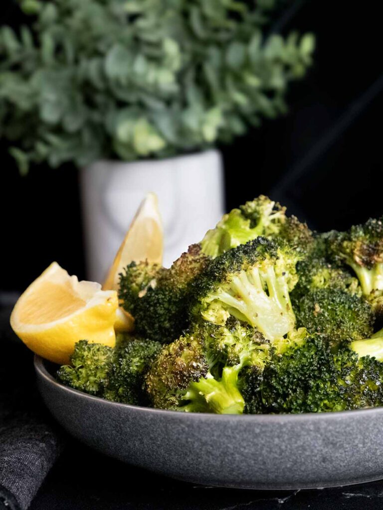 Roasted broccoli with lemon wedge garnish in a dark bowl.