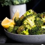 Roasted broccoli with lemon wedge garnish in a dark bowl.